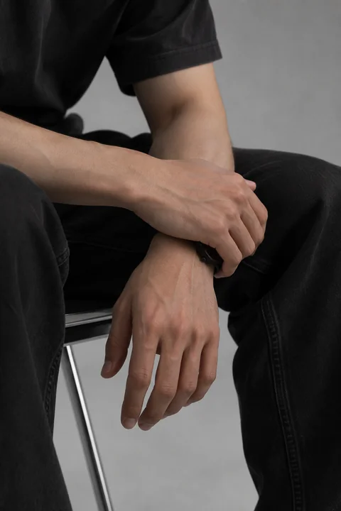 KAI seated, both hands resting together; full fingers and clothing detail
